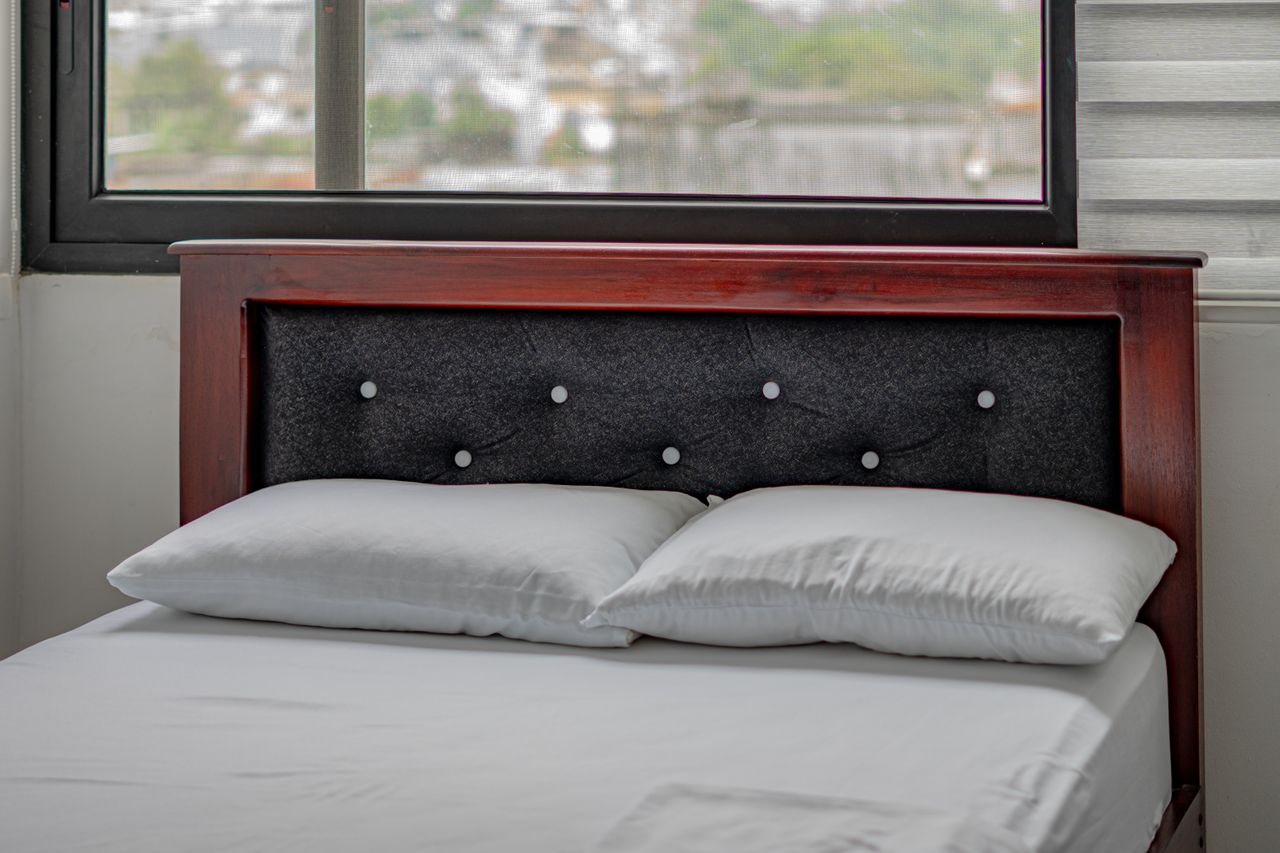 Services Modern bedroom with window view in Santo Domingo. Features a wooden headboard and comfortable bedding.