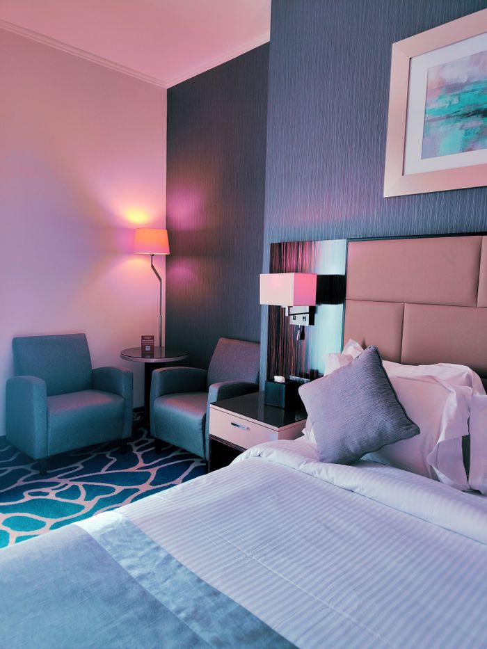 Services Stylishly lit hotel room with chairs, bedside table, and modern decor. Perfect for travelers.