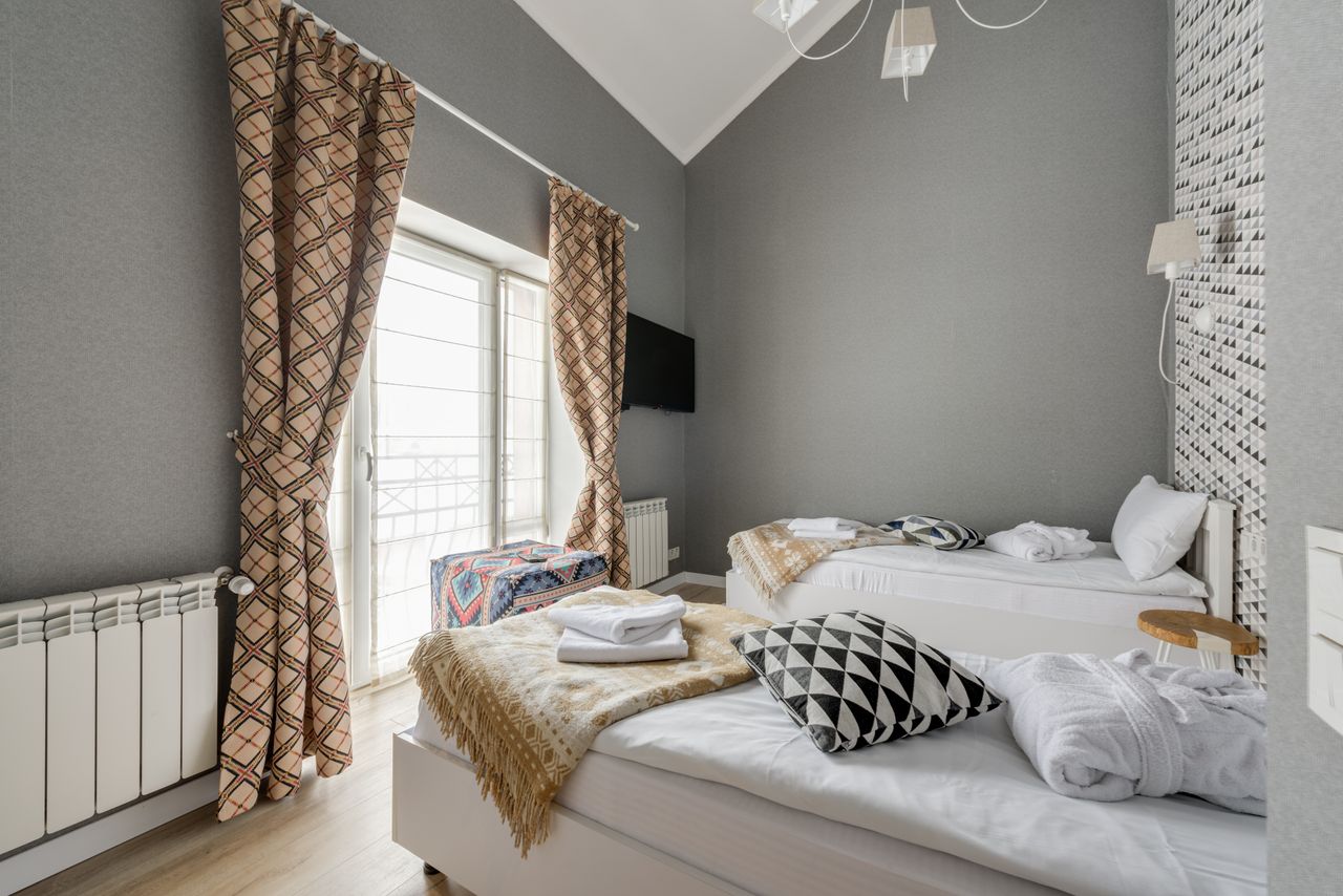 Services Stylish bedroom with twin beds, patterned curtains, and wall-mounted TV.